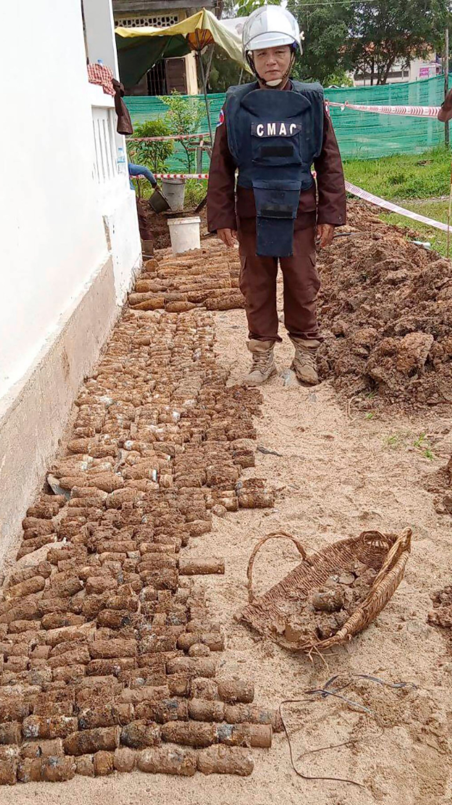 In this photo released by the Cambodia Mine Action Center, CMAC, a diminer expert stands near a pile of unexploded ordnances at Queen Kosamak Hight School in Kratie Province, northeastern of Phnom Penh, Cambodia, Sunday, Aug. 13, 2023. Cambodian authorities have temporarily closed the high school where thousands of pieces of unexploded ordinance from the country's nearly three decades of civil war have been unearthed. (Cambodia Mine Action Center via AP)